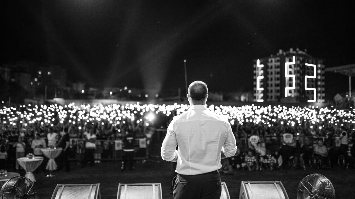 A performer faces a large crowd holding lights, capturing a moment of connection and excitement.